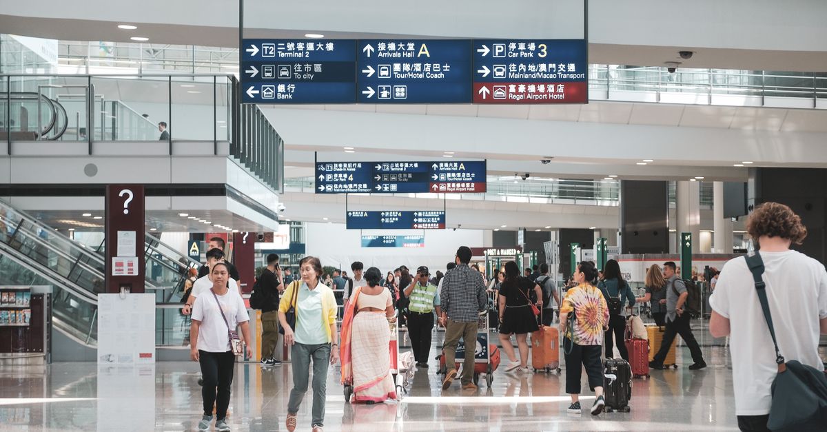 Terminal d'aéroport bondé à Hong Kong avec des passagers divers et des panneaux d'information.
